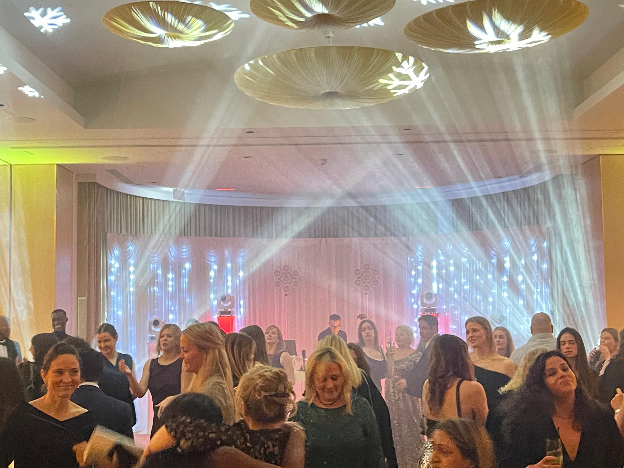 A packed ballroom dance floor with light beams cutting across the room