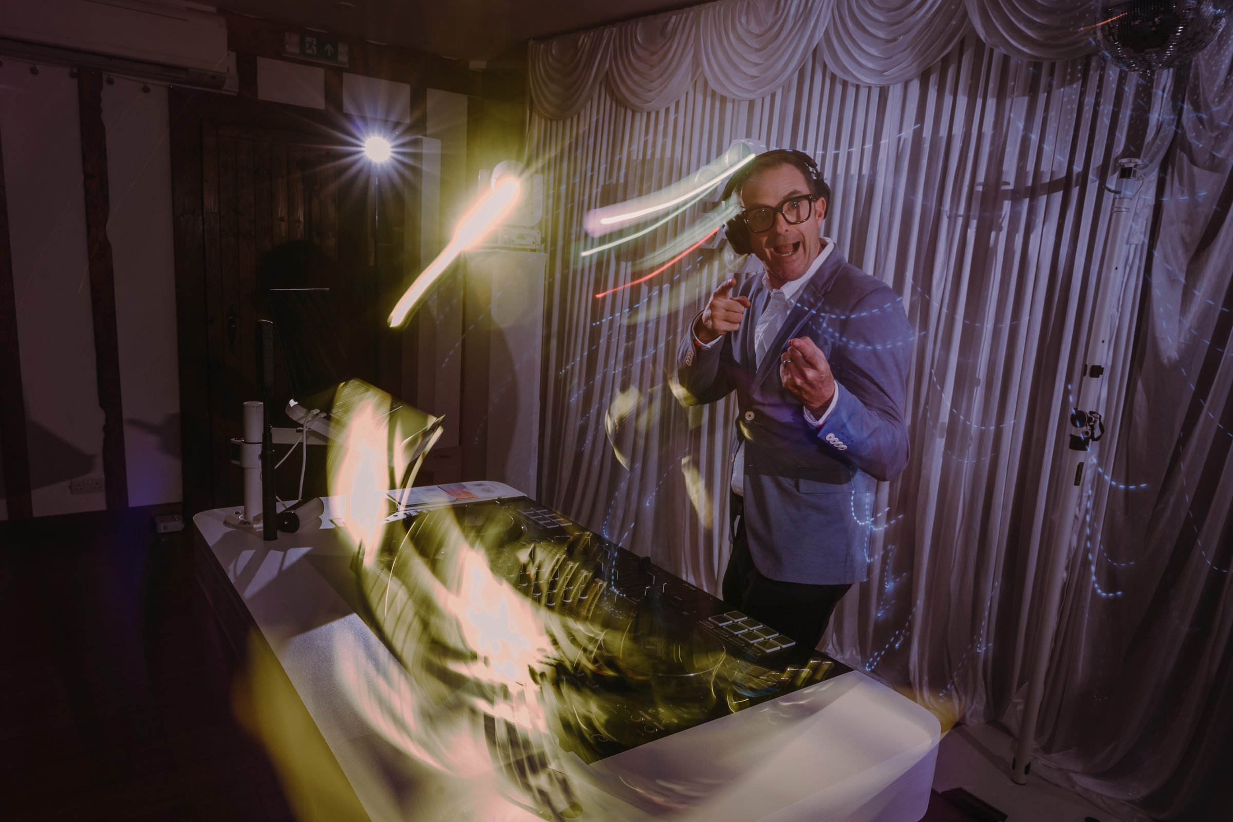 Matt behind the white booth, headphones on, pointing at the camera as light trails sweep across the frame