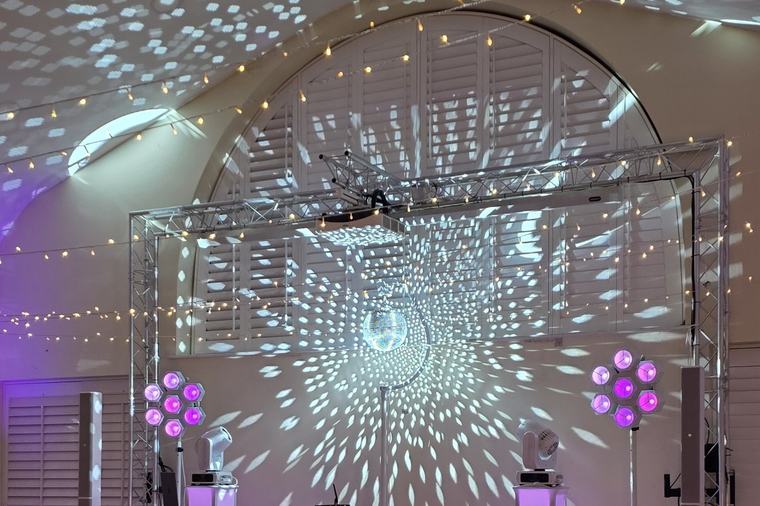 Mirror ball on truss scattering light across the arched room at Bennet's Club, with the DJ booth below