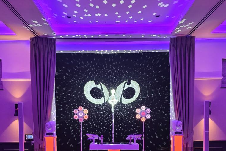 DJ booth against a lit backdrop at Denham Grove, with the room washed in purple uplighting