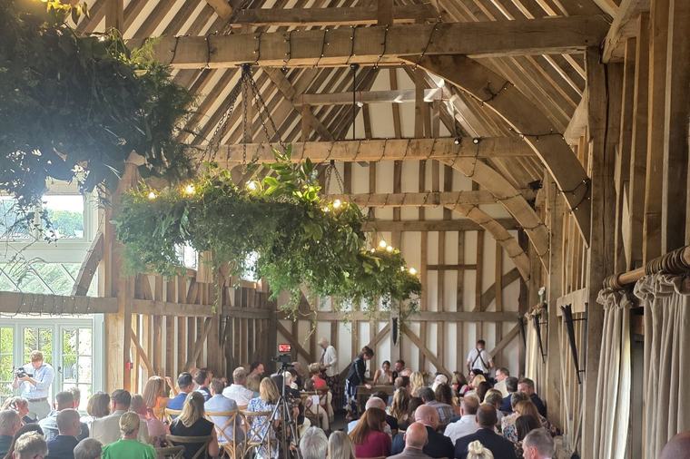The barn at Gate Street during a wedding ceremony, with guests seated under the oak roof and hanging foliage