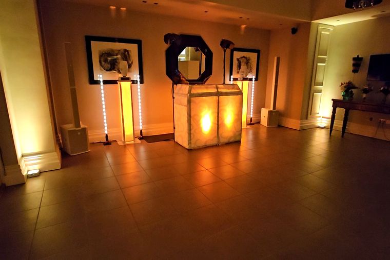 DJ booth lit warm amber in the tiled room at Talbooth House & Spa, with framed artwork and an octagonal mirror behind