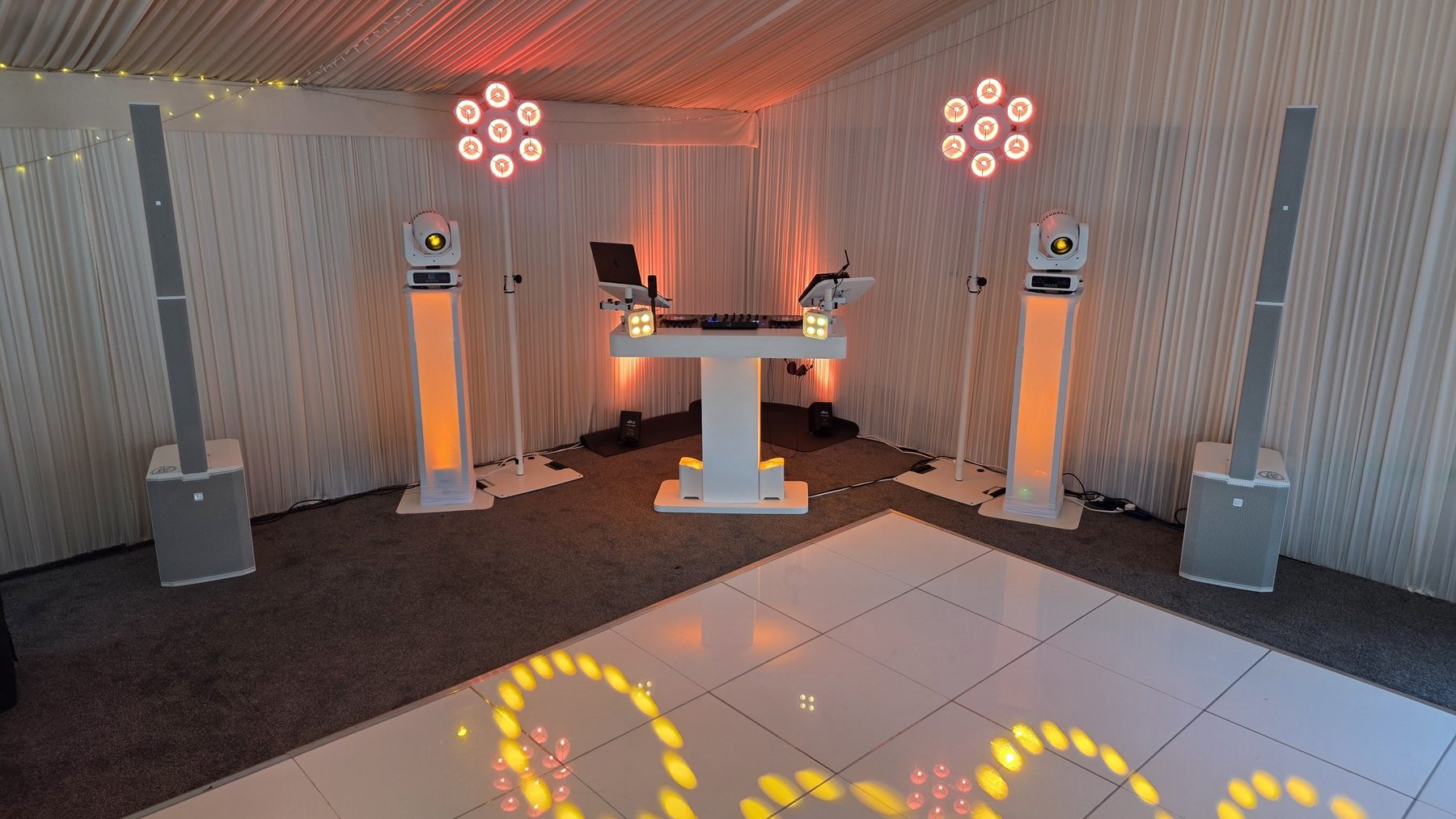 The white DJ Matty F booth with uplighting and a starlight backdrop in a draped marquee